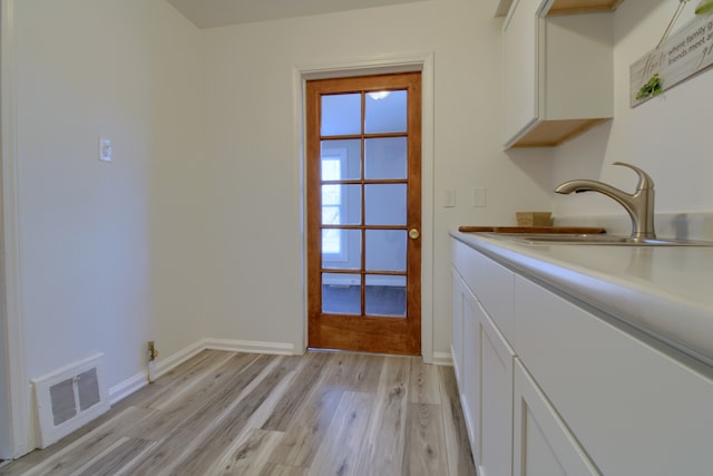 interior space featuring white cabinets, a sink, visible vents, and light wood-style floors