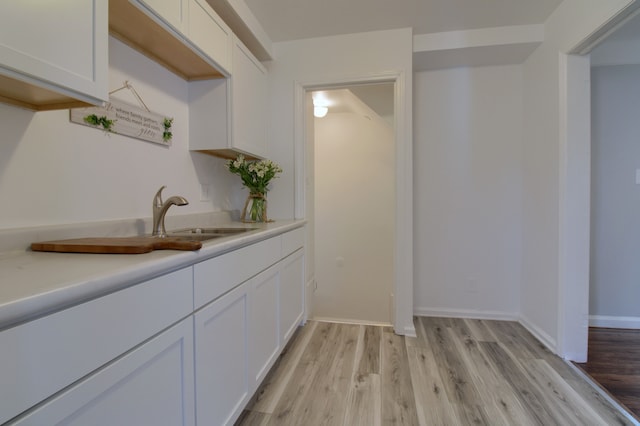 bar featuring light wood-type flooring, baseboards, and a sink