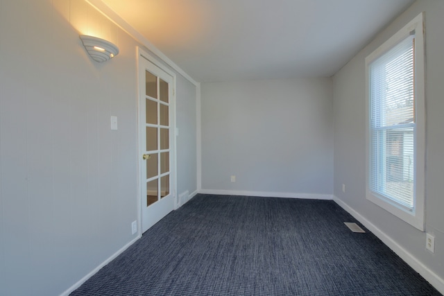 spare room featuring visible vents, baseboards, and dark colored carpet