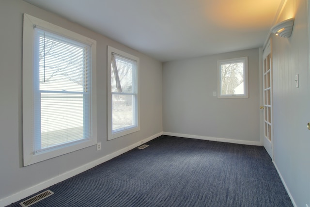 spare room with dark colored carpet, visible vents, and baseboards