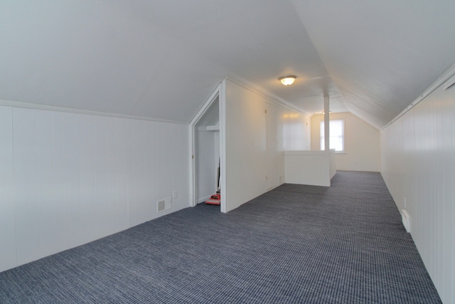 additional living space featuring visible vents, vaulted ceiling, and dark colored carpet