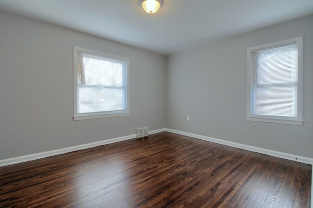 spare room with baseboards, visible vents, and dark wood-style flooring