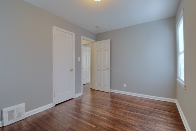 empty room featuring dark wood finished floors, visible vents, and baseboards