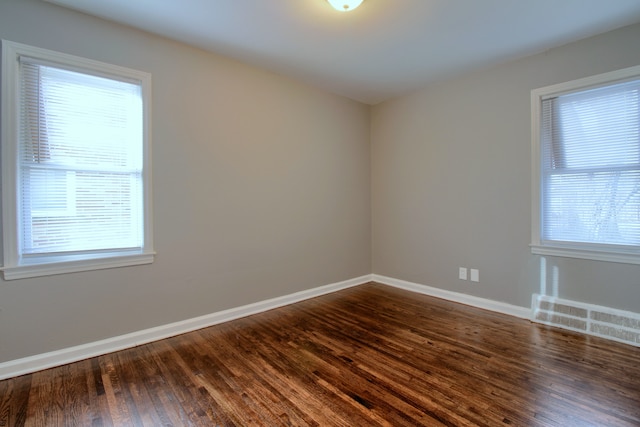 empty room featuring visible vents, baseboards, and dark wood finished floors