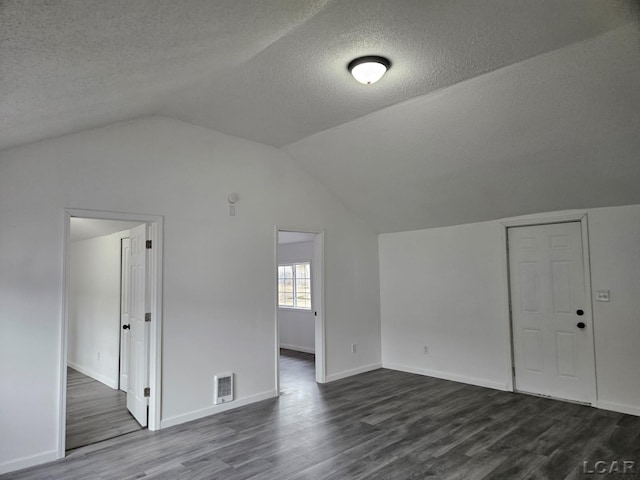 additional living space with a textured ceiling, dark wood-type flooring, visible vents, baseboards, and vaulted ceiling