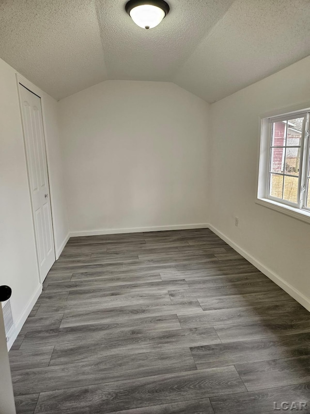 interior space with lofted ceiling, a textured ceiling, wood finished floors, baseboards, and a closet