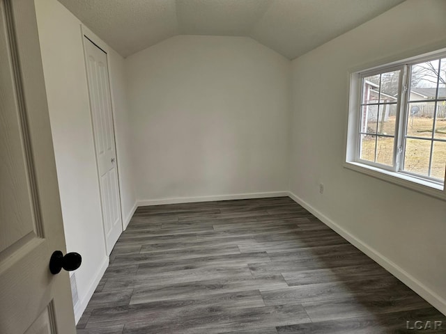 empty room featuring lofted ceiling, a textured ceiling, dark wood-style floors, and baseboards