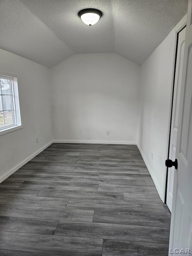 empty room featuring lofted ceiling, a textured ceiling, dark wood finished floors, and baseboards