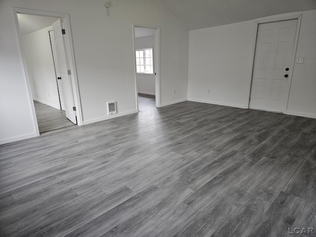 spare room with dark wood-style floors, vaulted ceiling, visible vents, and baseboards