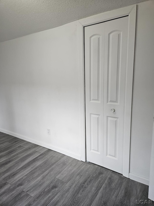 unfurnished bedroom with dark wood-style floors, a closet, a textured ceiling, and baseboards