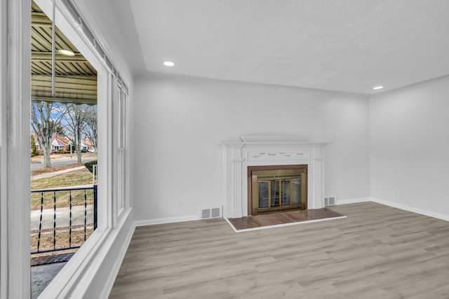 unfurnished living room with recessed lighting, visible vents, a glass covered fireplace, wood finished floors, and baseboards