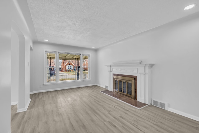 unfurnished living room featuring arched walkways, visible vents, a glass covered fireplace, wood finished floors, and baseboards