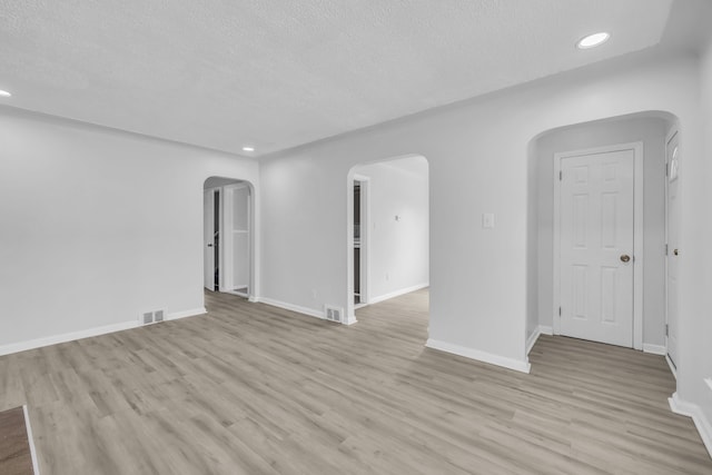 spare room featuring baseboards, visible vents, arched walkways, a textured ceiling, and light wood-type flooring