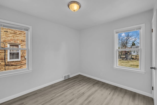 empty room with light wood-style flooring, visible vents, and baseboards