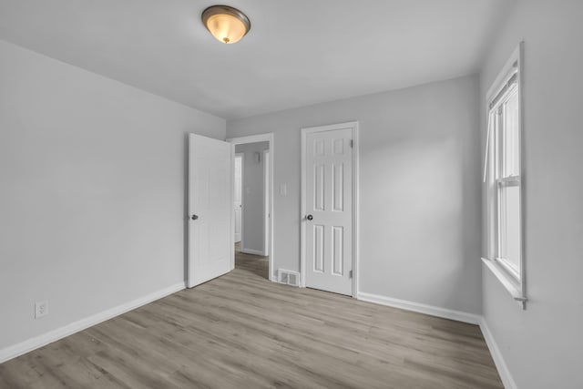 unfurnished bedroom with a closet, visible vents, baseboards, and wood finished floors