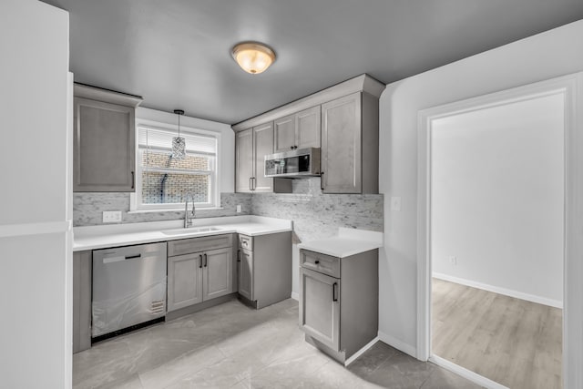 kitchen featuring pendant lighting, gray cabinets, backsplash, appliances with stainless steel finishes, and a sink