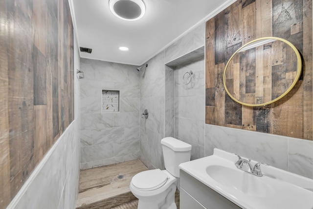 full bath with tiled shower, vanity, toilet, and tile walls