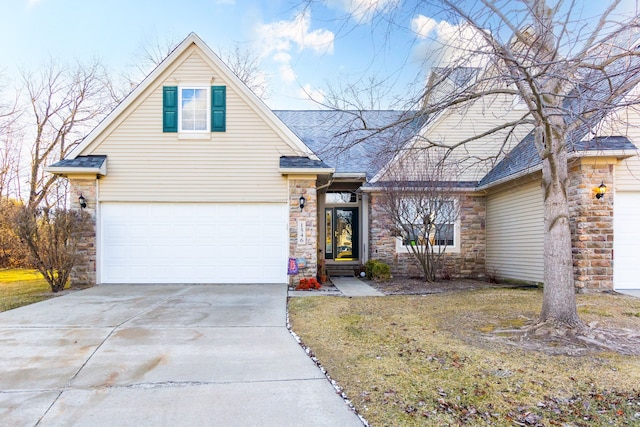 traditional-style home with a front yard, roof with shingles, an attached garage, concrete driveway, and stone siding