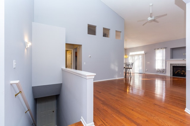 unfurnished living room with wood finished floors, baseboards, high vaulted ceiling, a fireplace with flush hearth, and ceiling fan