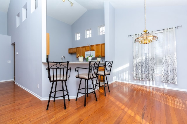 kitchen with white microwave, baseboards, a kitchen bar, wood finished floors, and brown cabinetry