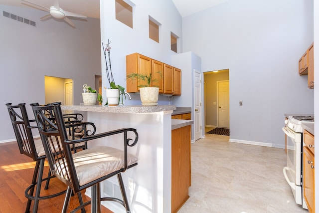 kitchen with visible vents, white range with gas cooktop, a breakfast bar, light countertops, and ceiling fan