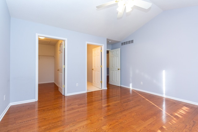 unfurnished bedroom featuring wood finished floors, visible vents, baseboards, vaulted ceiling, and a spacious closet