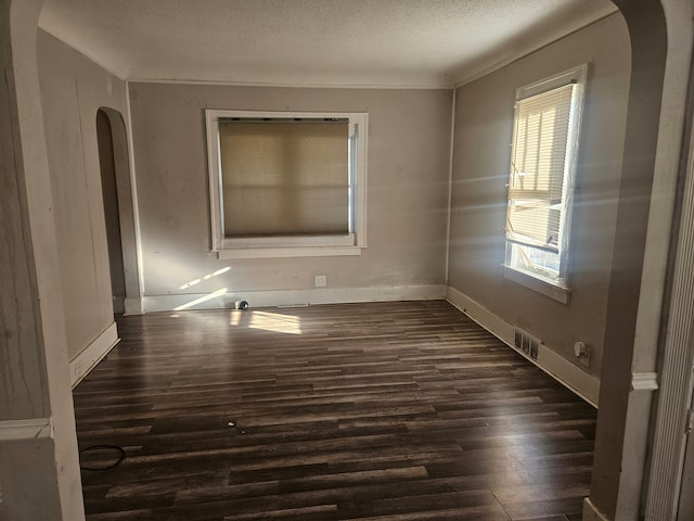 empty room featuring baseboards, a textured ceiling, arched walkways, and dark wood-style flooring