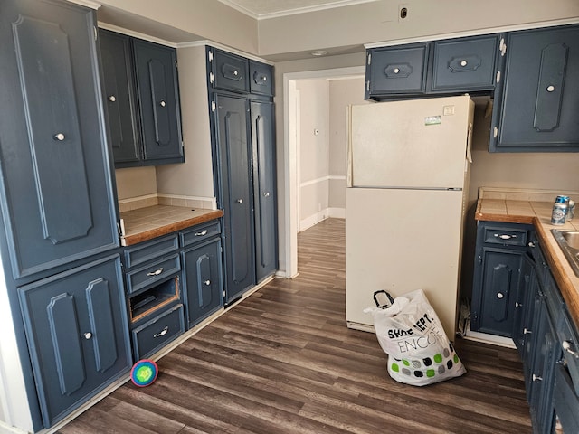 kitchen with dark wood-style flooring, baseboards, tile counters, freestanding refrigerator, and crown molding