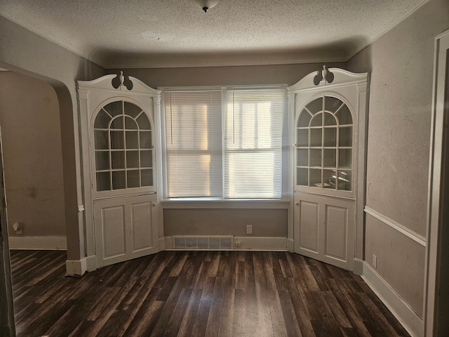 unfurnished dining area featuring baseboards, visible vents, arched walkways, dark wood-style flooring, and a textured ceiling