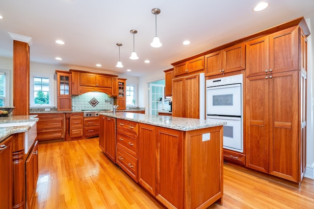 kitchen with double oven, a wealth of natural light, light wood finished floors, brown cabinetry, and glass insert cabinets