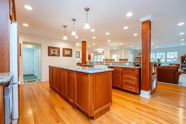 kitchen with brown cabinetry, open floor plan, plenty of natural light, and ornate columns