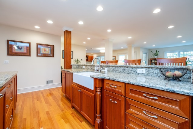 kitchen with a healthy amount of sunlight, ornate columns, light wood-style flooring, and a sink