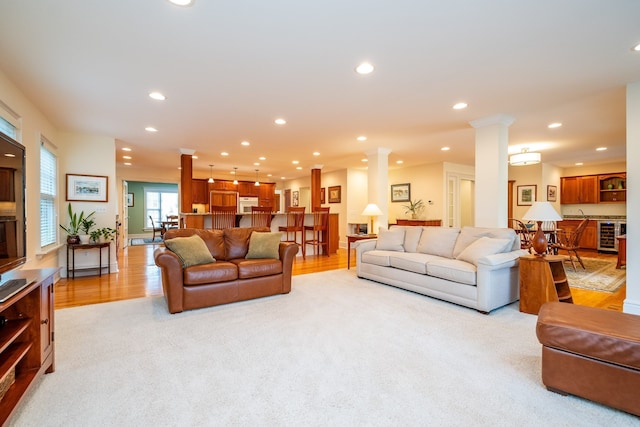 living room with light wood-style floors, recessed lighting, beverage cooler, and decorative columns