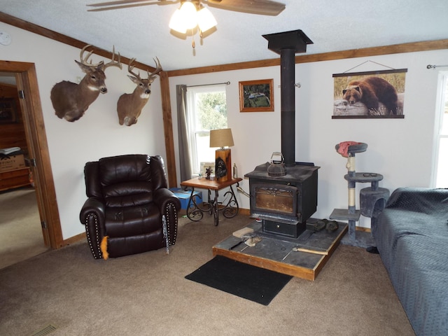 carpeted living area featuring ceiling fan, a textured ceiling, baseboards, a wood stove, and crown molding