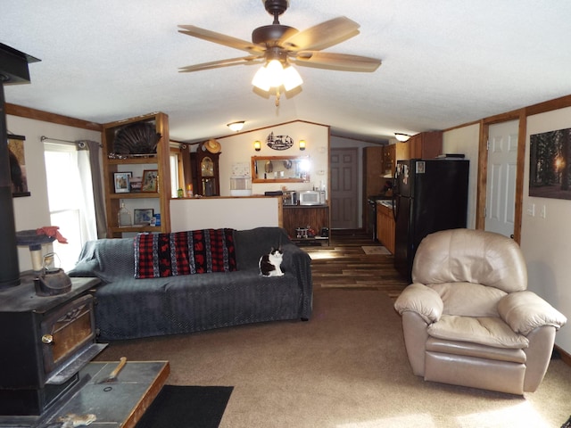 carpeted living area featuring vaulted ceiling, a wood stove, and a ceiling fan