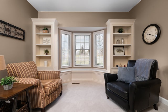 living area with built in features, visible vents, baseboards, and light colored carpet