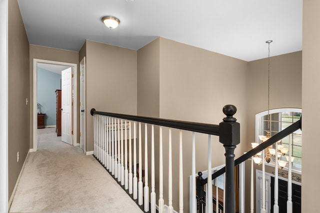 corridor with an upstairs landing, a chandelier, baseboards, and carpet