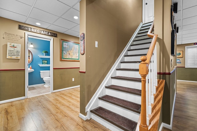 stairs featuring wood finished floors, baseboards, and a paneled ceiling