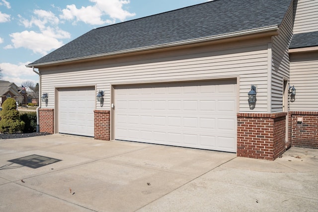 view of property exterior with concrete driveway, a garage, brick siding, and roof with shingles