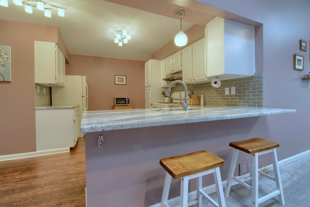 kitchen featuring white cabinets, a sink, a peninsula, and decorative backsplash