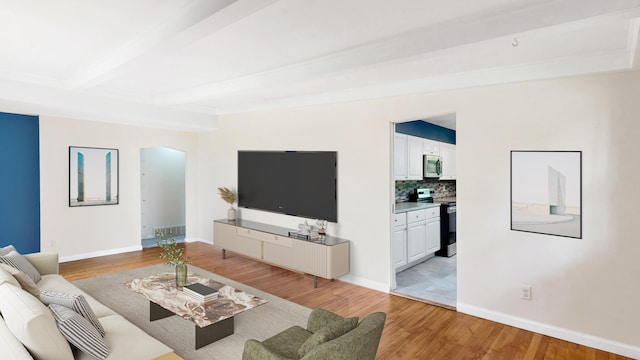 living room with light wood-style floors, baseboards, arched walkways, and beam ceiling