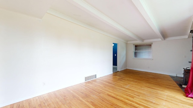 empty room with wood finished floors, visible vents, baseboards, beamed ceiling, and a wood stove