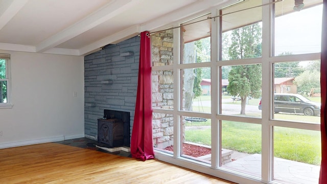 unfurnished living room with vaulted ceiling with beams, wood finished floors, a wood stove, and baseboards