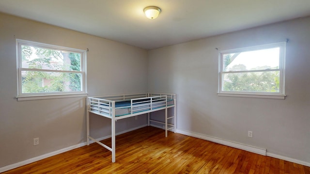 unfurnished bedroom featuring multiple windows, baseboards, and wood finished floors