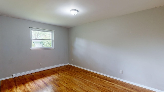 empty room featuring a baseboard radiator, wood-type flooring, and baseboards