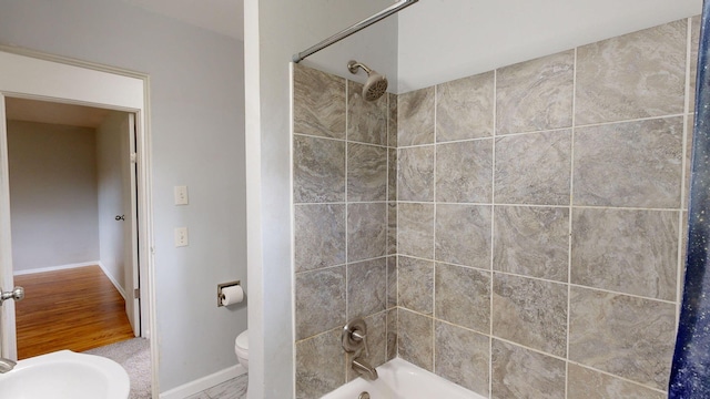 bathroom with toilet, washtub / shower combination, baseboards, and a sink