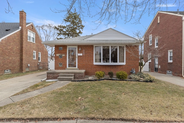 bungalow with a shingled roof, brick siding, and a front lawn