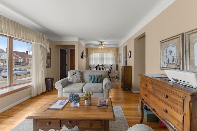 living room featuring ceiling fan, light wood-style floors, baseboards, and a healthy amount of sunlight