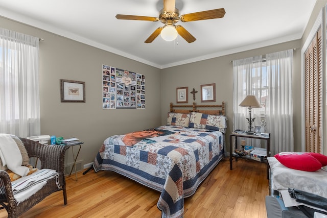 bedroom with baseboards, wood-type flooring, ceiling fan, crown molding, and a closet