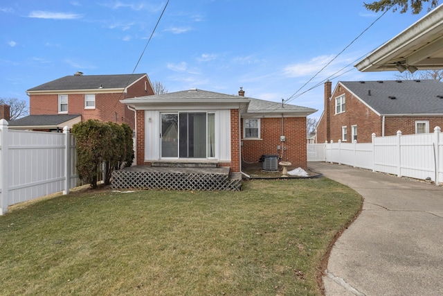 rear view of house featuring entry steps, central AC unit, fence private yard, brick siding, and a lawn